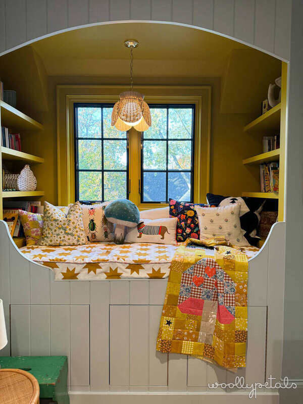 Cozy window seat nook with mustard yellow walls, built-in shelving, and patterned pillows and quilt