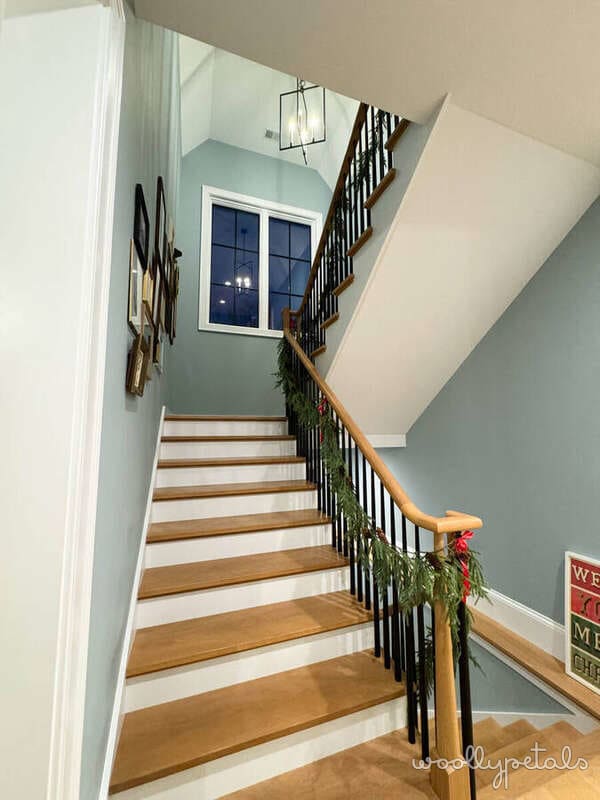 Staircase with wood steps, white risers, black railing, and sage green walls