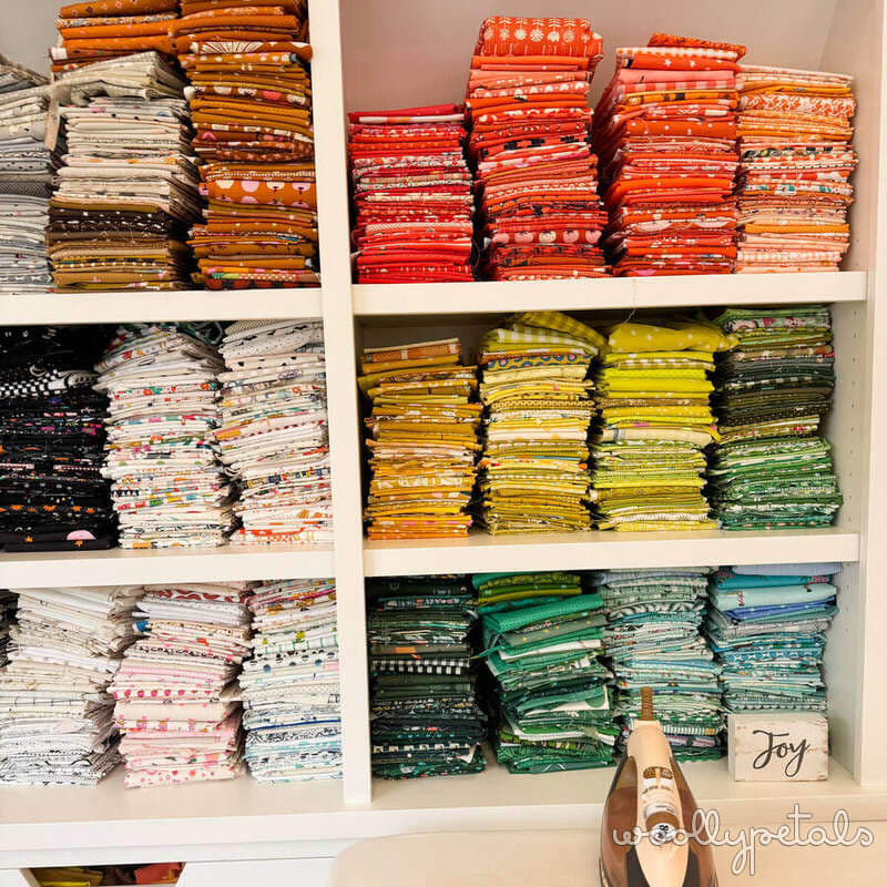 Organized fabric stash on white shelving with coordinated color groups