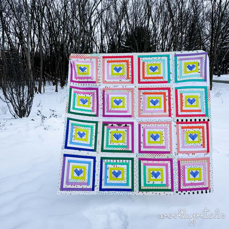 Woollypetals Clogged quilt displayed in snow with colorful concentric heart blocks