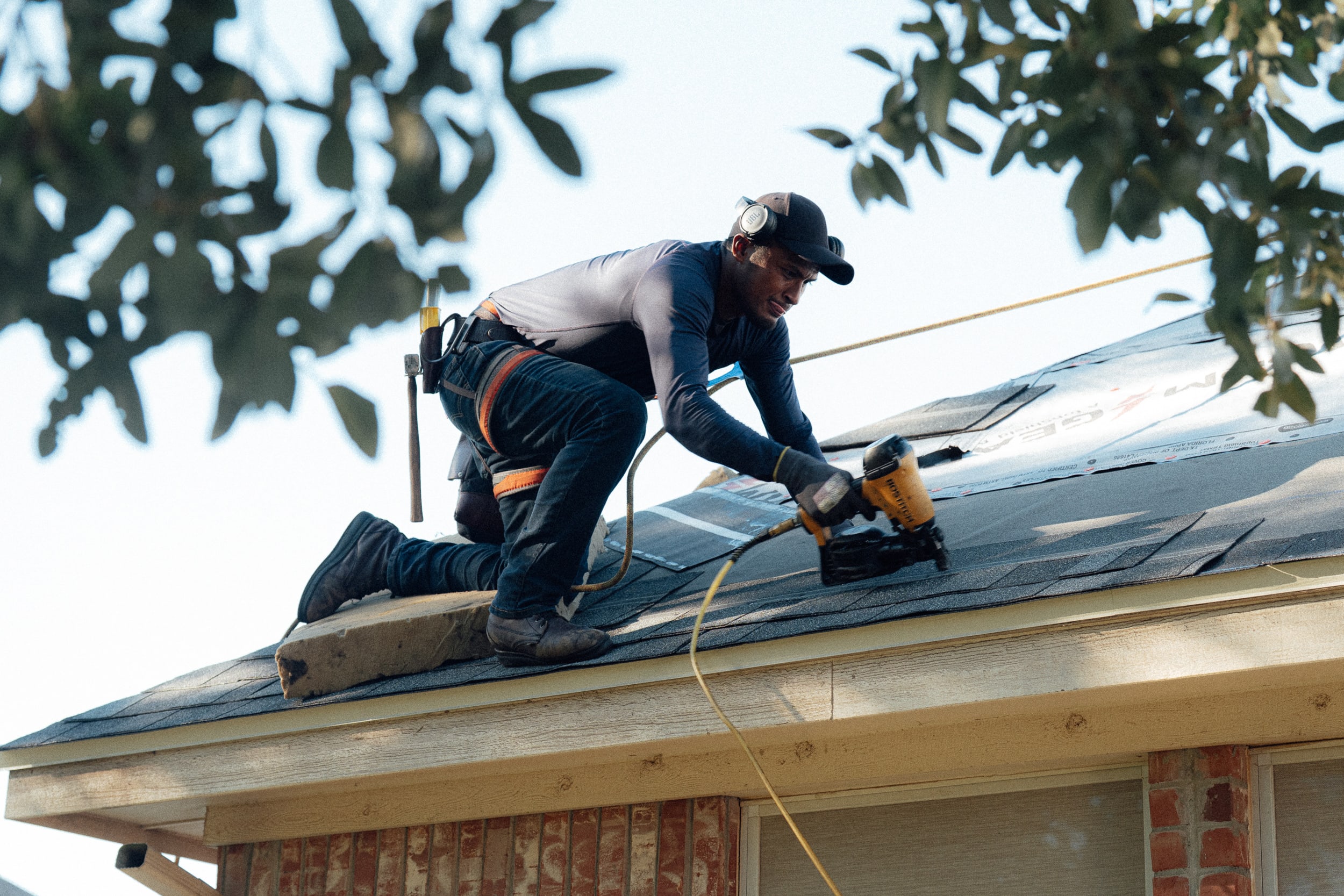 A roofer nailing down shingles along the edge of a roof