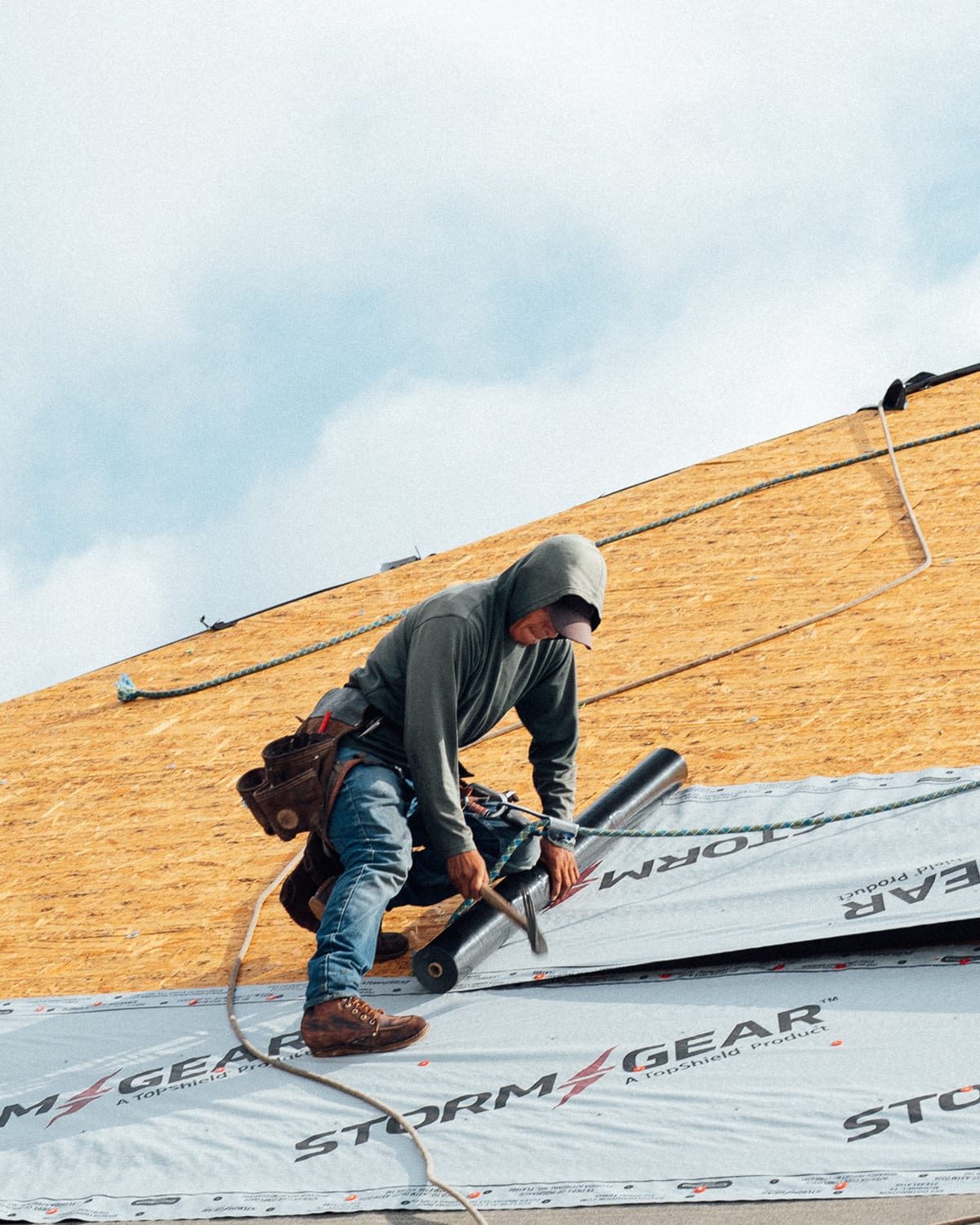 A roofer rolling out underlayment across a roof deck