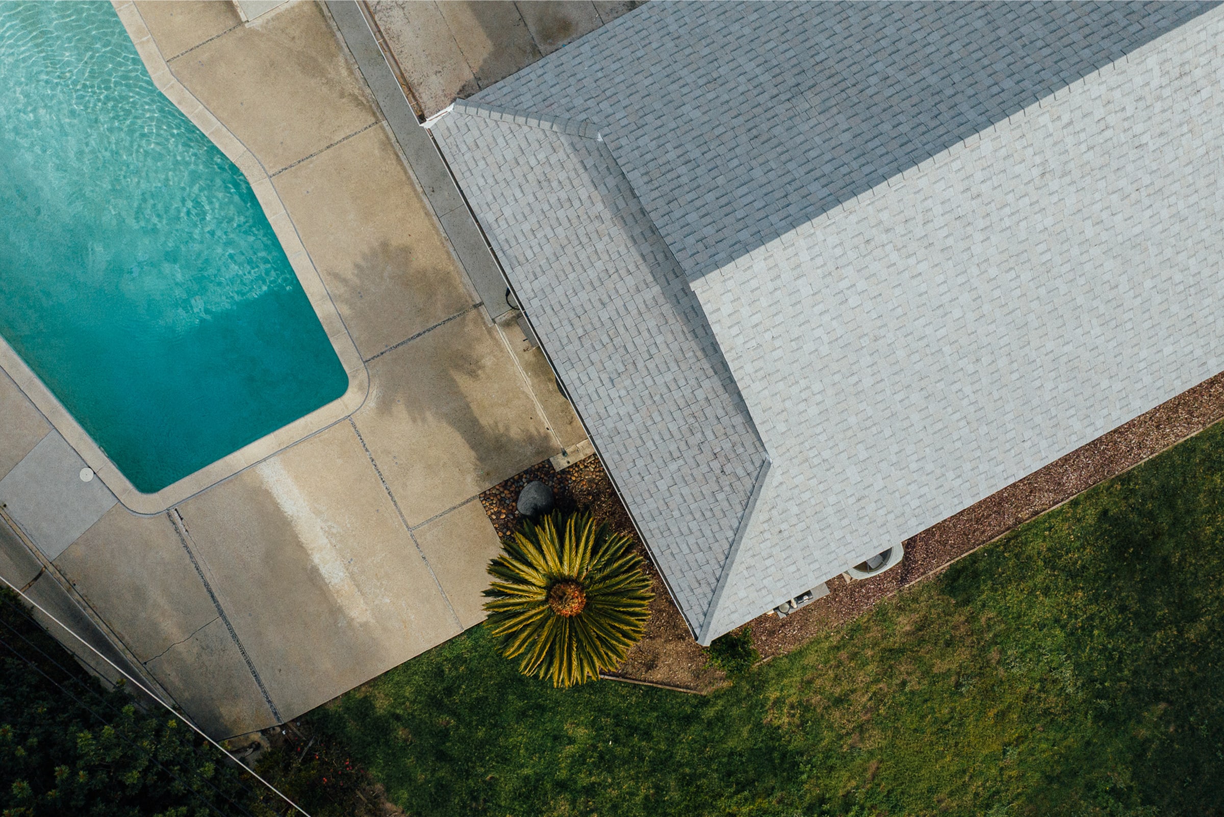 An aerial view of a gray shingle roof beside a backyard pool