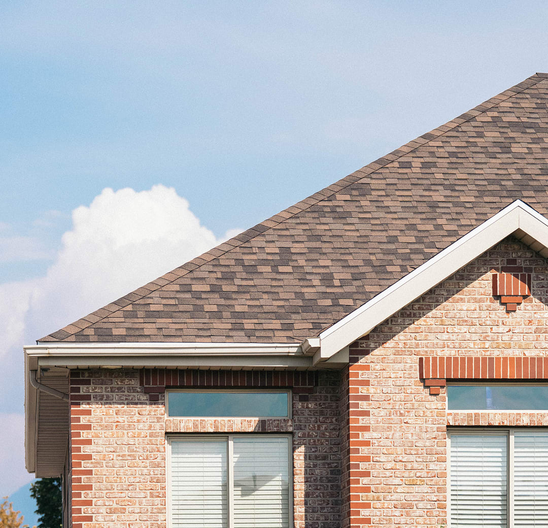 A brown shingle roof over a brick home