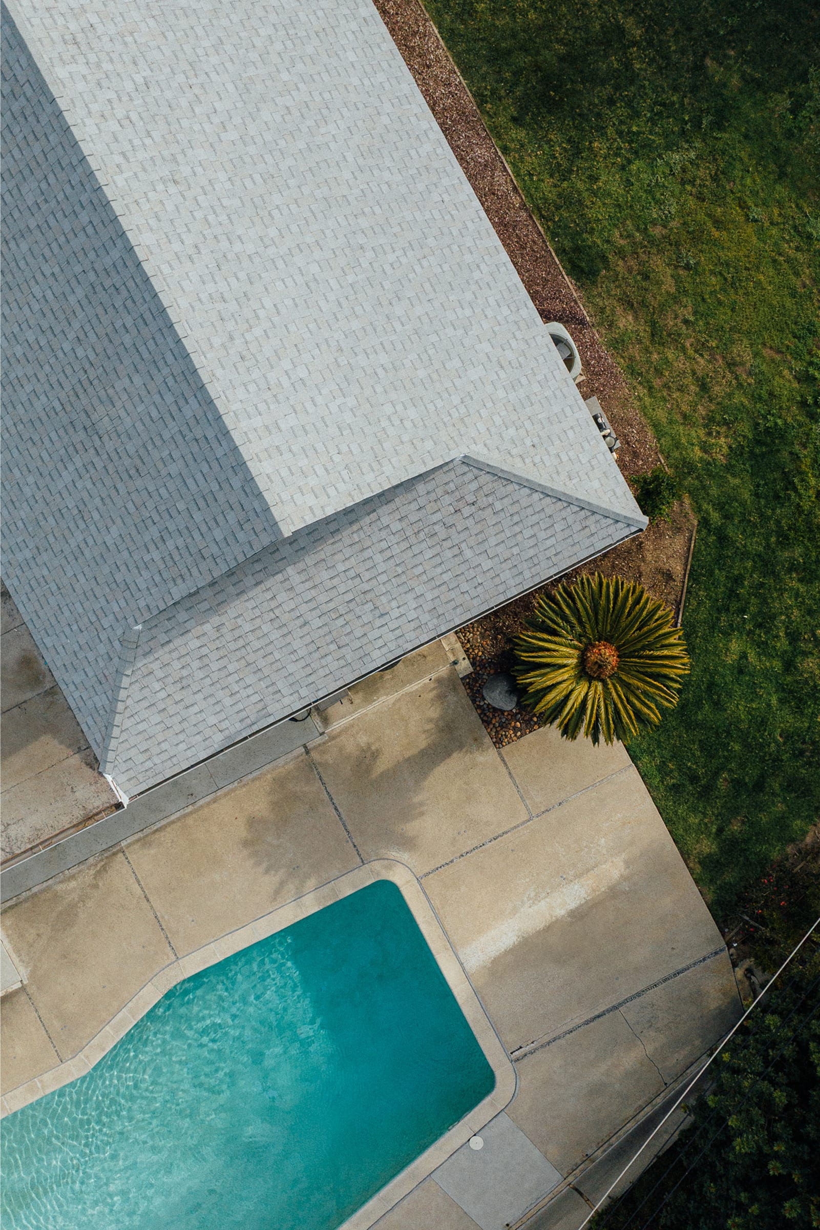 An aerial view of a gray shingle roof beside a backyard pool