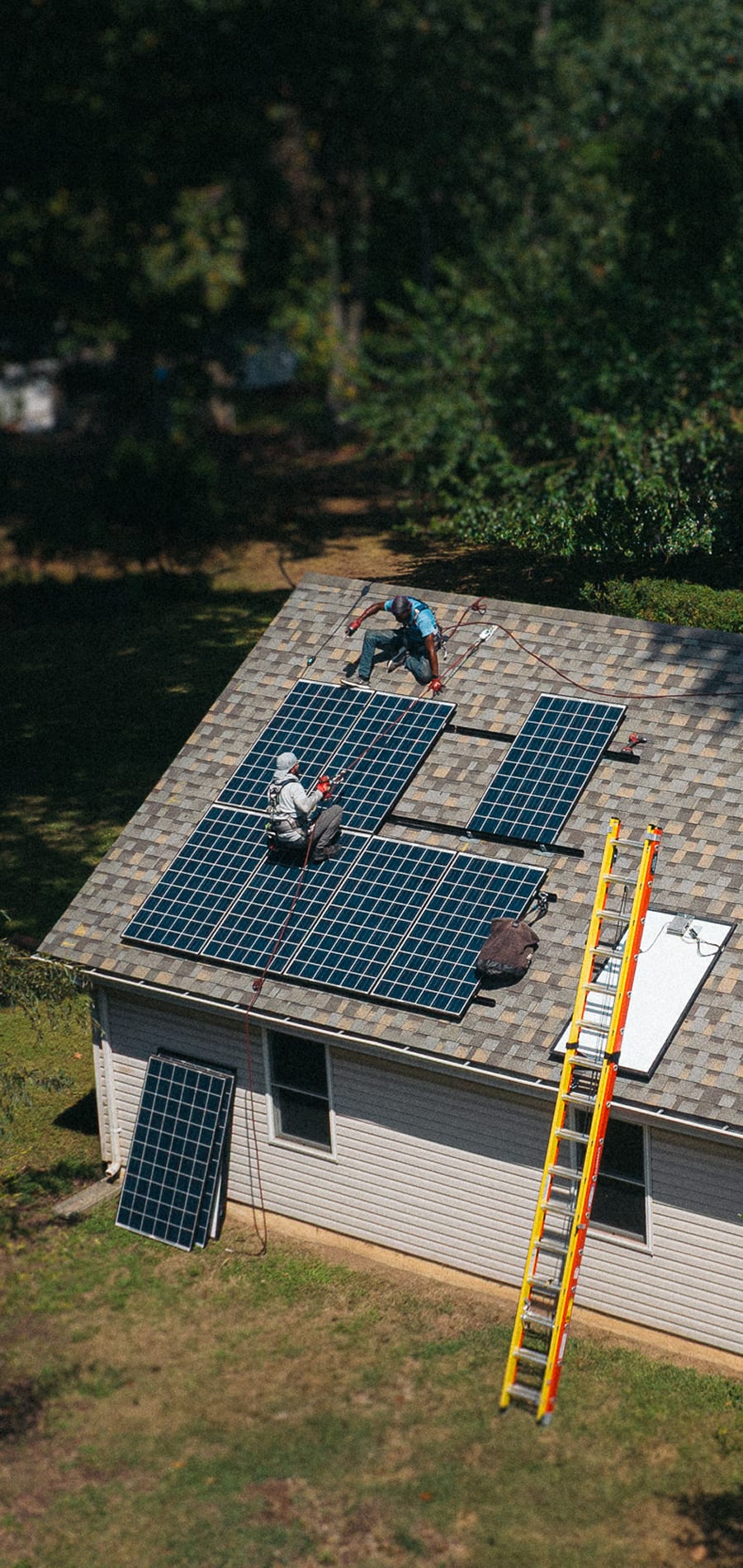 An aerial view of two installers mounting panels on a roof, ladder against the eave