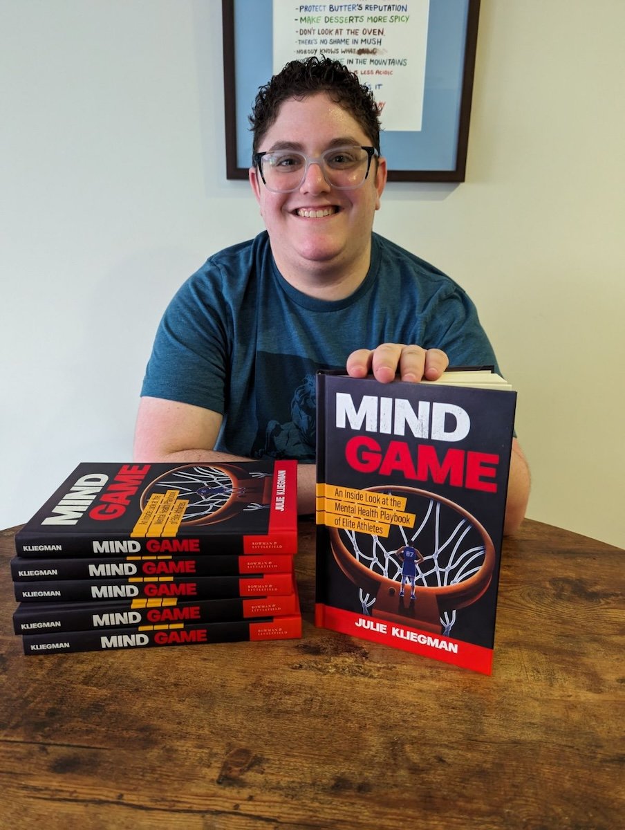 Julie Kliegman smiling and posing with a stack of Mind Game copies