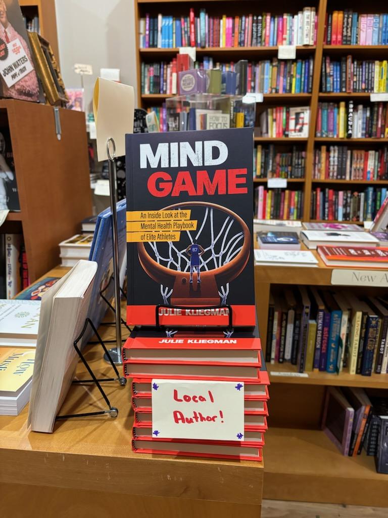 A stack of Mind Game copies at Astoria Bookshop with a sign reading “local author”