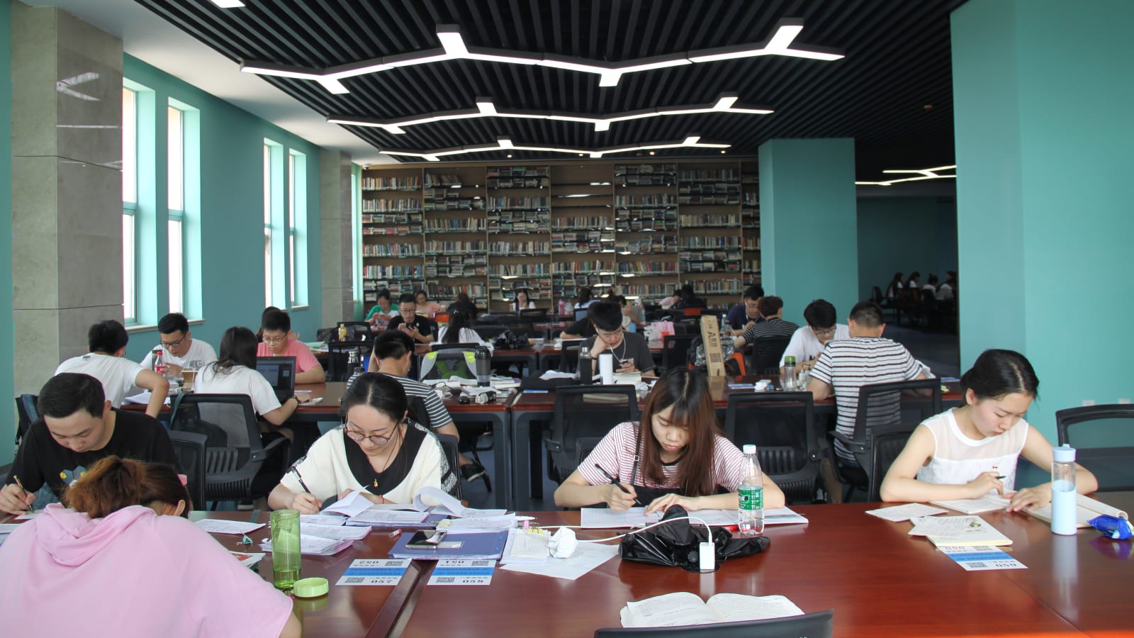 Sala de estudio de una biblioteca universitaria con estudiantes trabajando en mesas largas y estanterías de libros al fondo