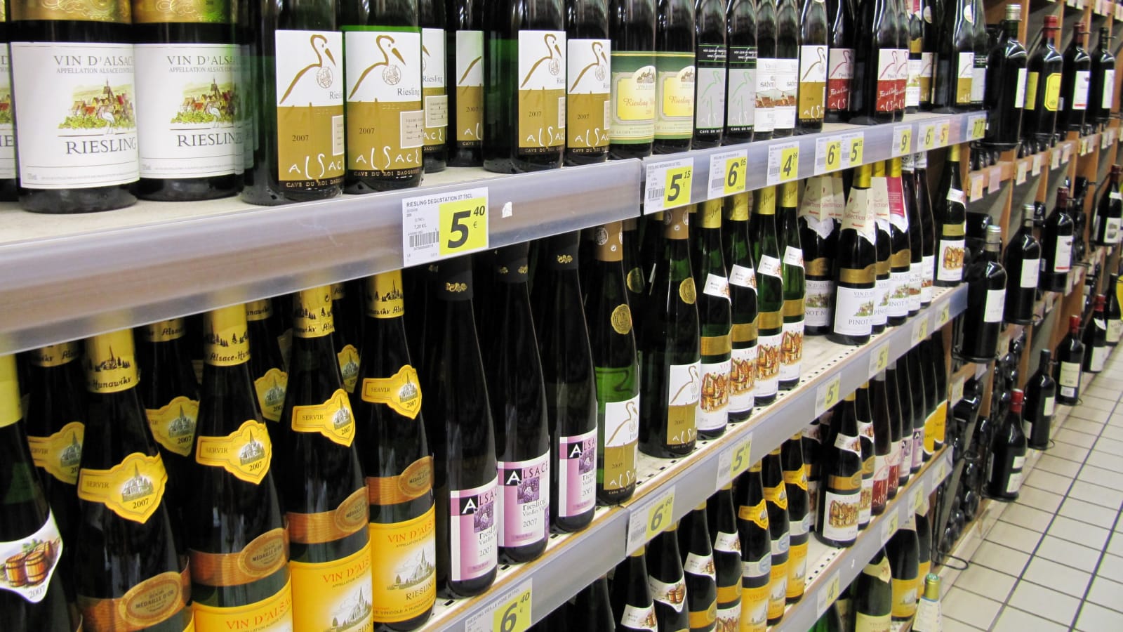 Lineal de un supermercado europeo con botellas de vino de Alsacia ordenadas en varias baldas y etiquetas de precio en euros