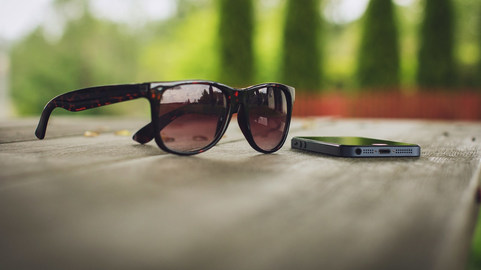 Unas gafas de sol y un teléfono móvil sobre una mesa de madera al aire libre