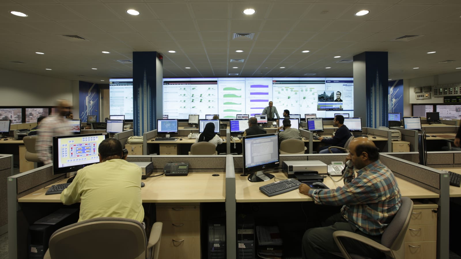 Centro de operaciones de red con técnicos frente a pantallas de monitorización y un videowall al fondo