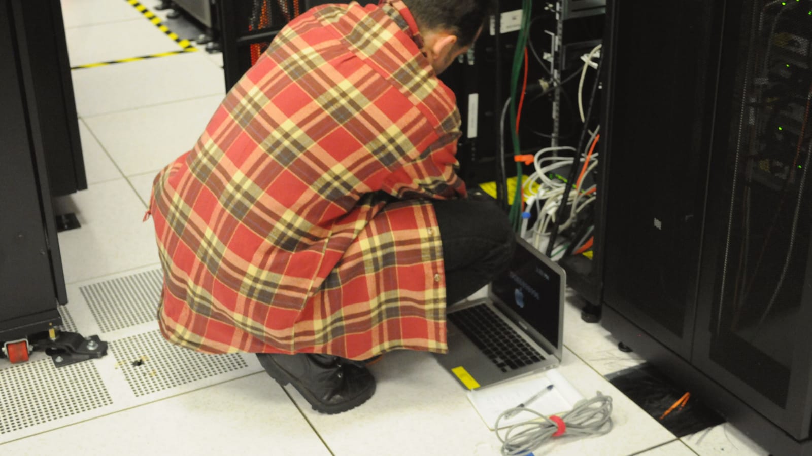 Técnico trabajando con un portátil frente a un rack de servidores en un centro de datos
