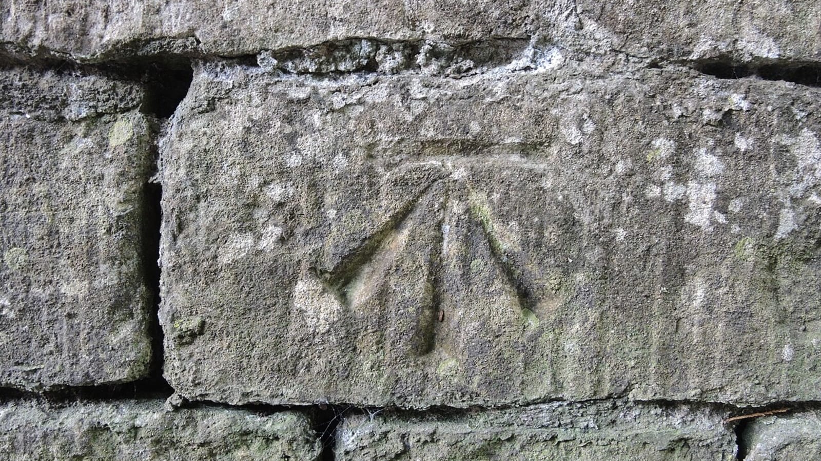Marca de nivelación de topógrafo, una flecha bajo una raya horizontal, grabada en un muro de piedra