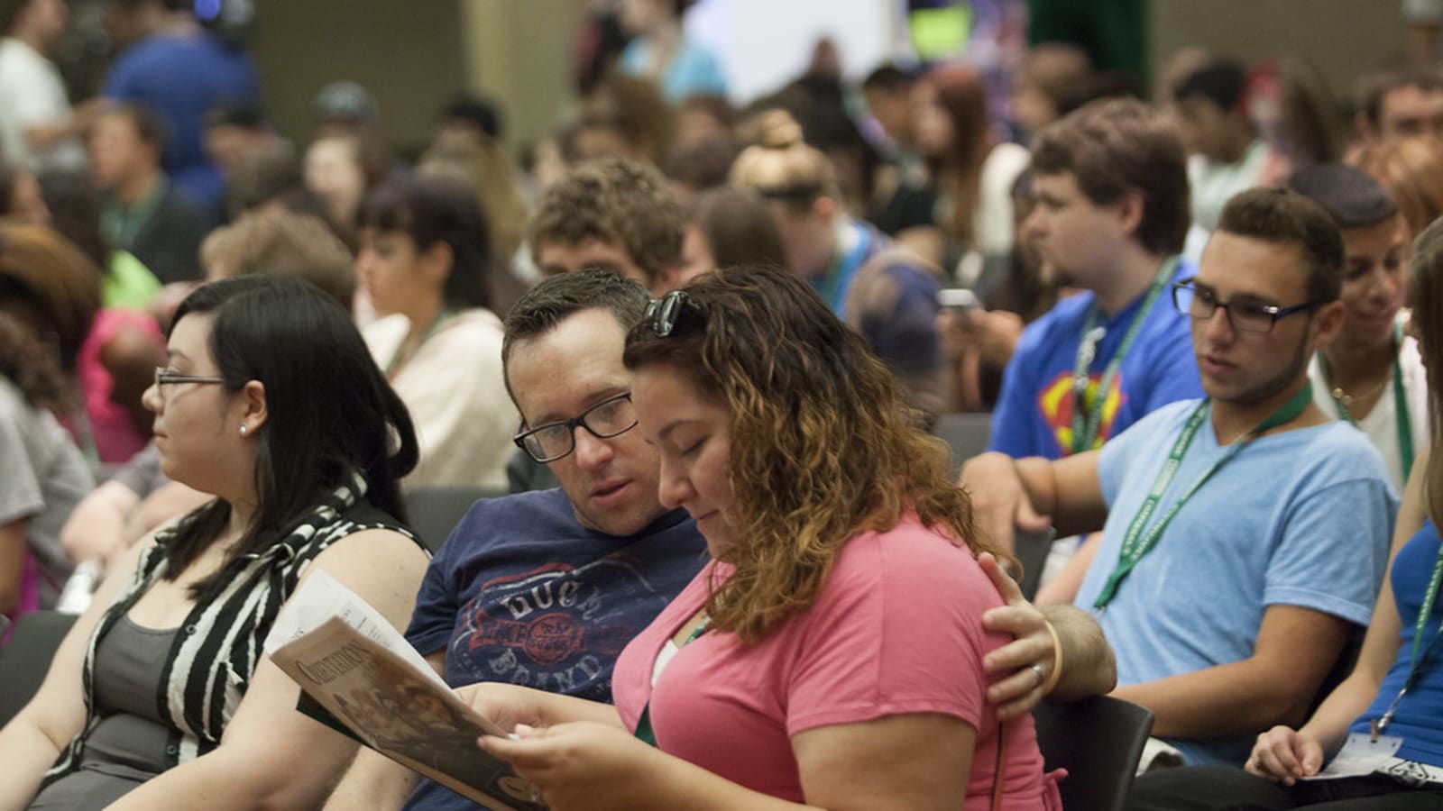Estudiantes sentados en una sesión de bienvenida universitaria, una de ellas leyendo un folleto