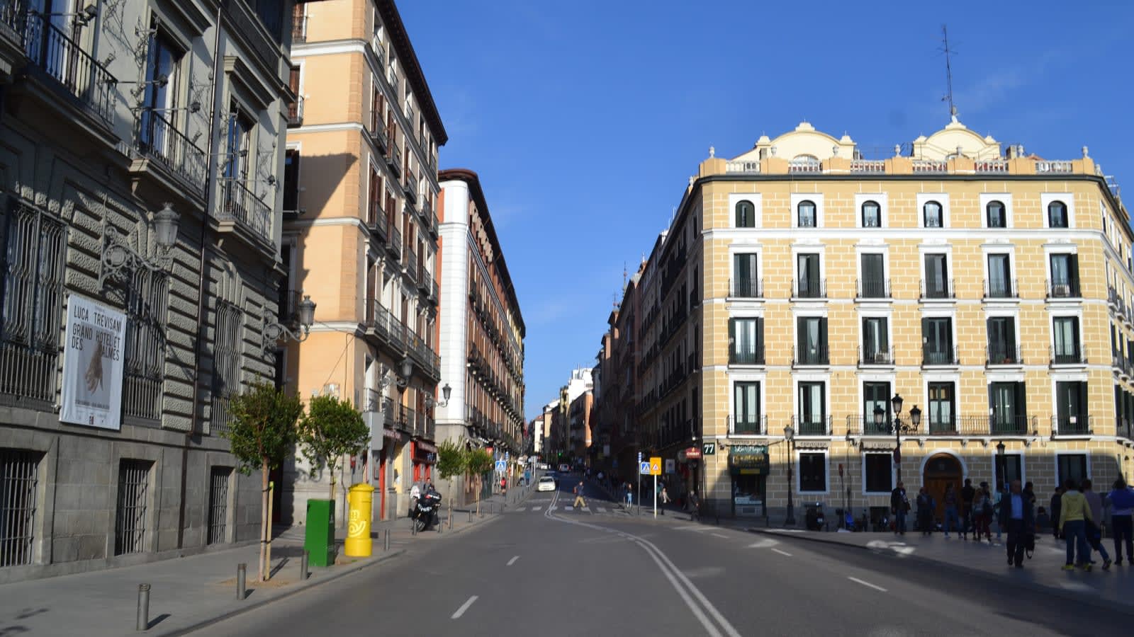 Calle Mayor de Madrid con edificios y una lona publicitaria en una fachada, vista hacia el centro
