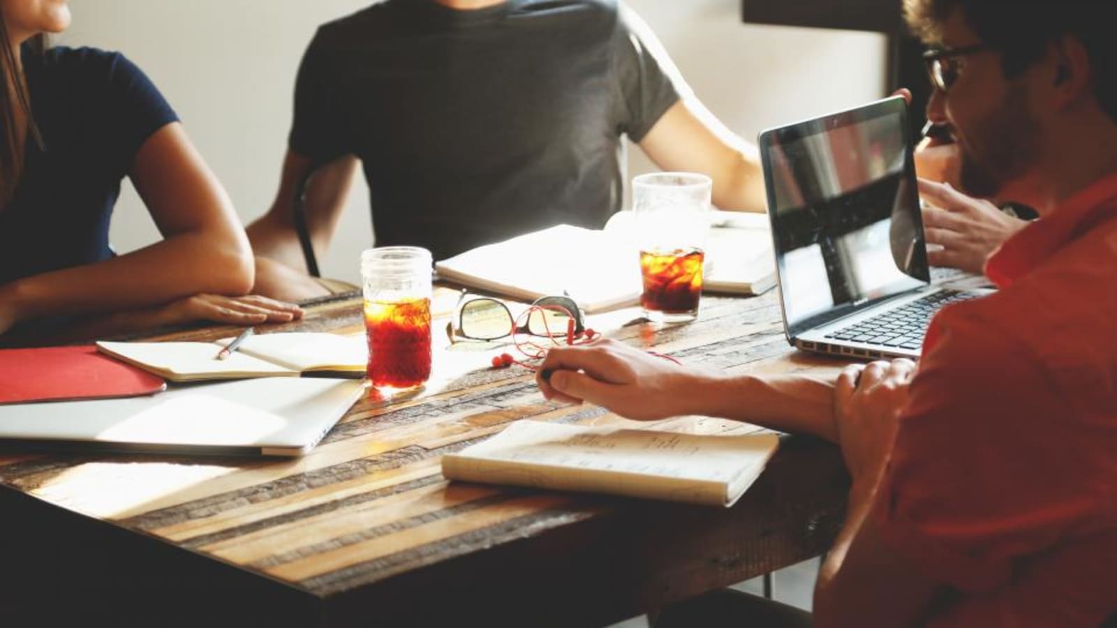 Equipo de trabajo reunido alrededor de una mesa de madera con portátiles, libretas y bebidas, tomando notas