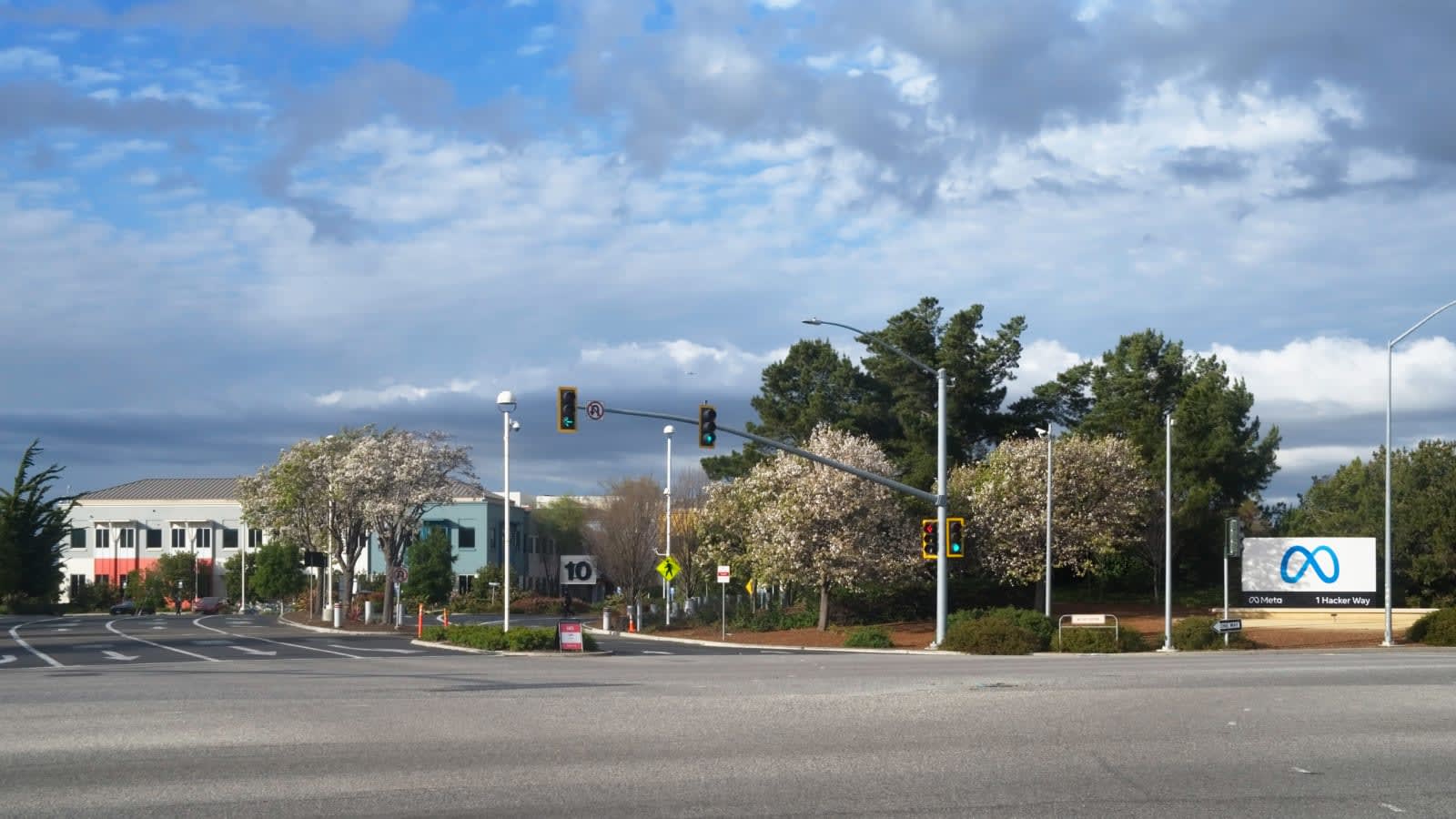 Entrada a la sede de Meta en Menlo Park (California), con el cartel del logotipo de Meta y la dirección 1 Hacker Way junto a un cruce con semáforos