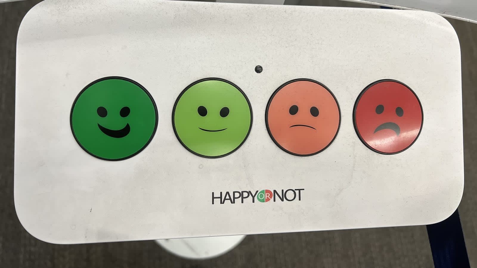 Terminal de valoración de clientes con cuatro botones de caras, de la verde sonriente a la roja triste, en el aeropuerto de San Francisco