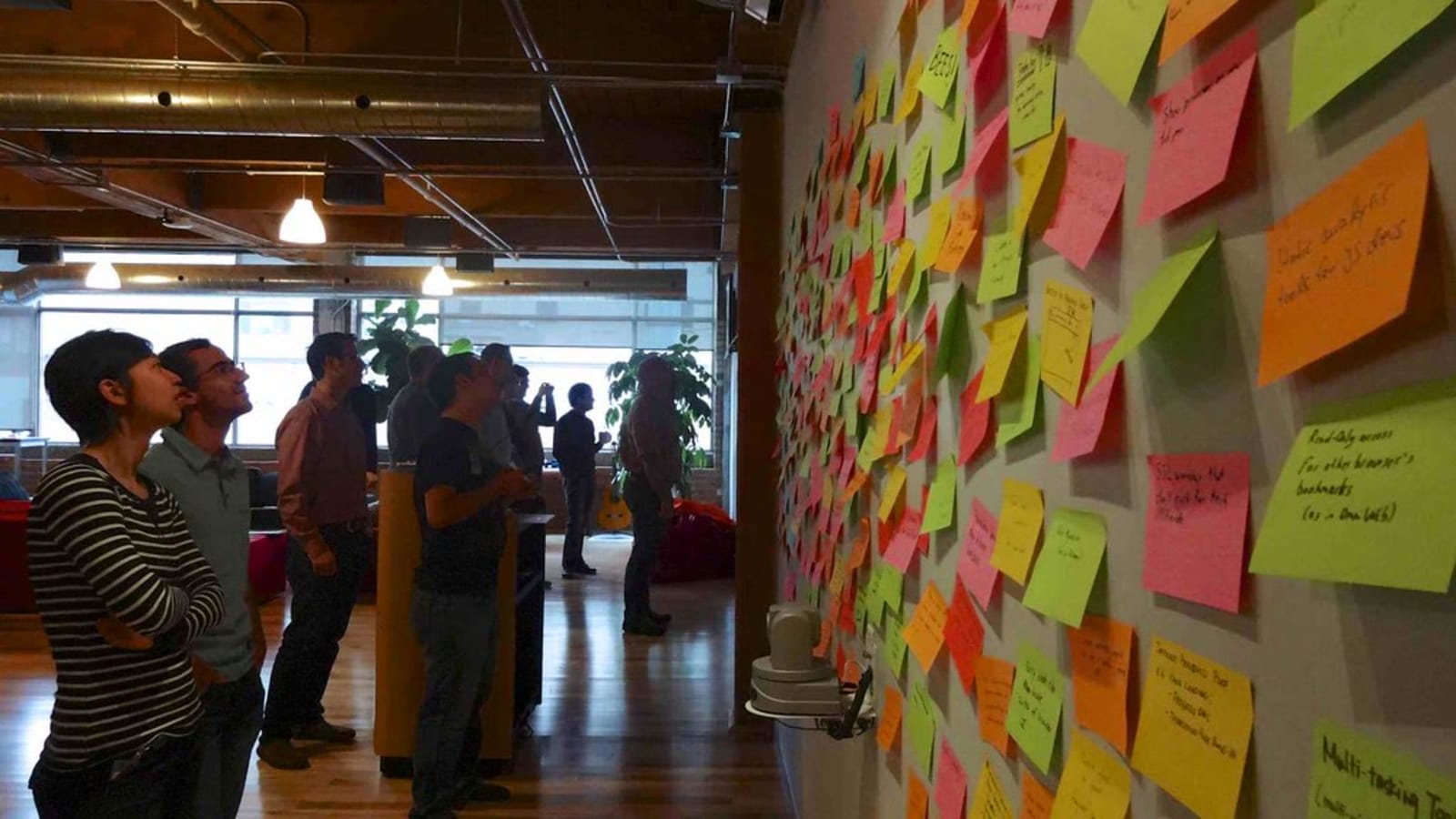 Un grupo de personas observa una pared cubierta de notas adhesivas de colores en una oficina