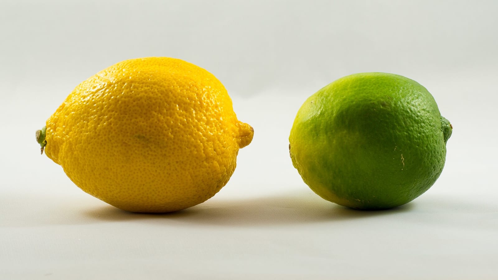 Un limón amarillo y una lima verde colocados uno junto al otro sobre fondo blanco