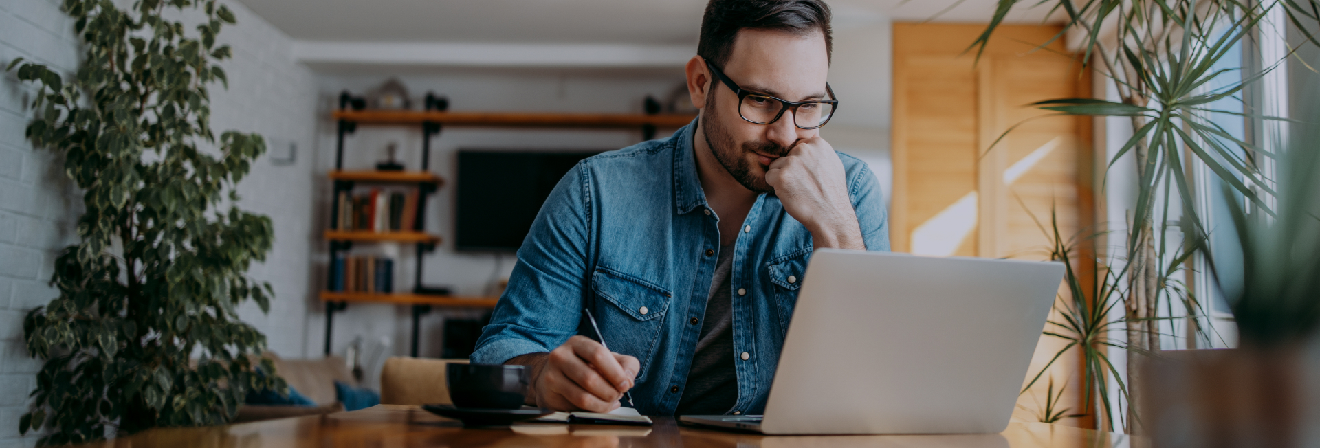 Man in glasses looking at laptop while making notes