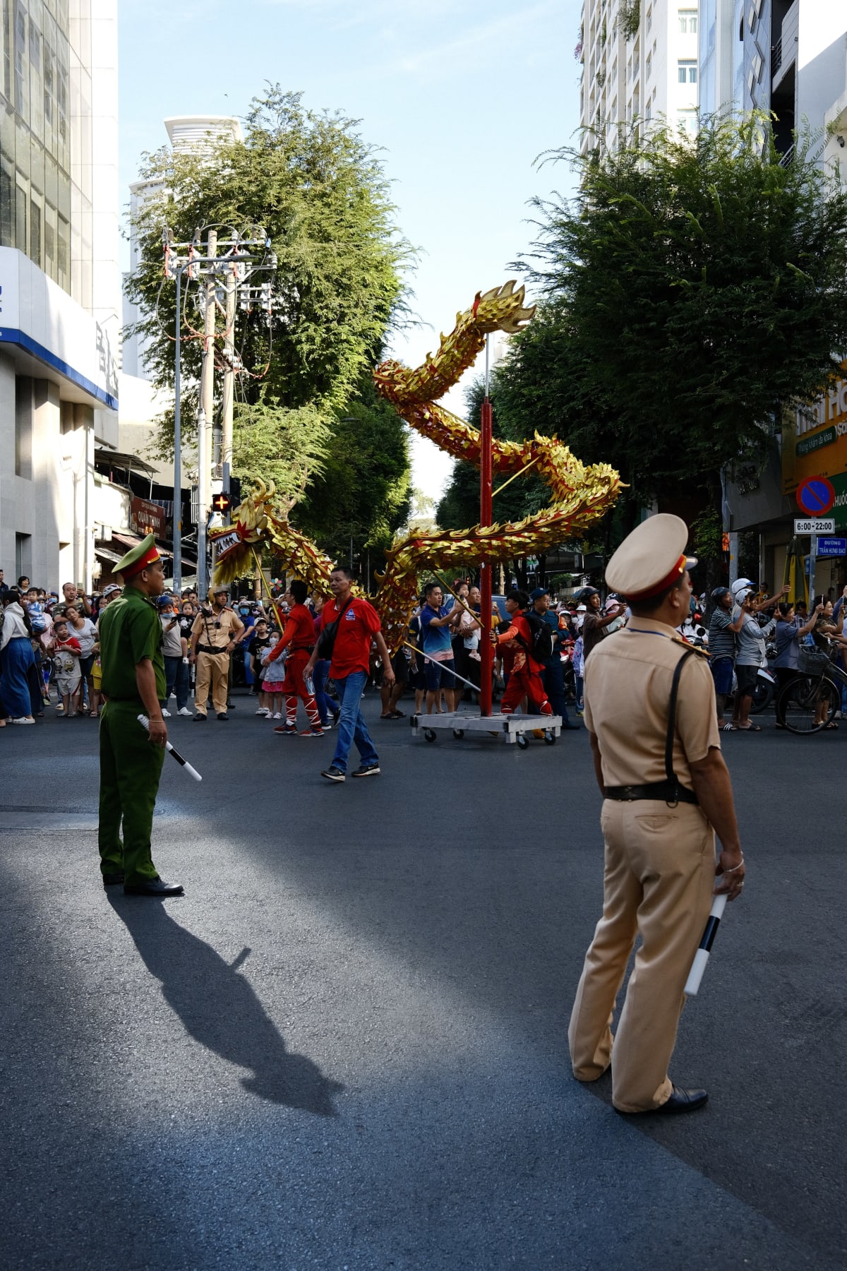 Two traffic officers watch from the middle of the road as a golden dragon rears over a crowded street performance — Luke Neville