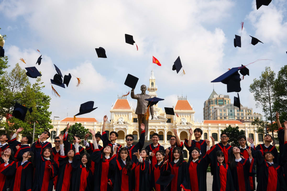 Graduates in red and black gowns throw their caps into the sky in front of Saigon's City Hall — Luke Neville