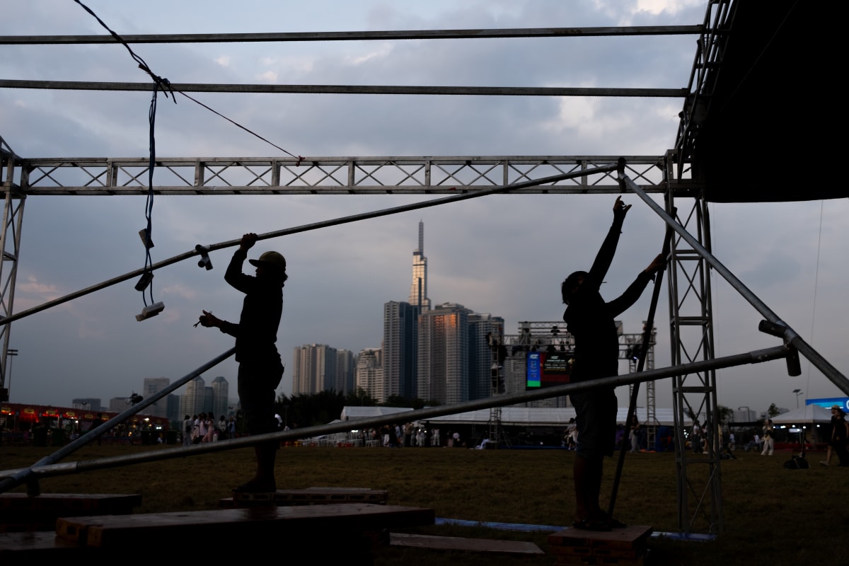 Two riggers hoist scaffold poles at dusk, silhouetted against Landmark 81 and the Saigon skyline — Luke Neville