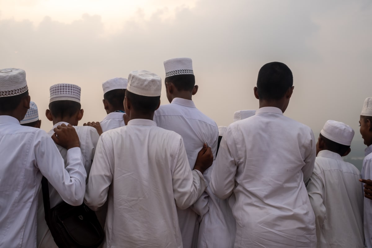 Boys in white robes and prayer caps stand shoulder to shoulder, looking out into the haze — Luke Neville