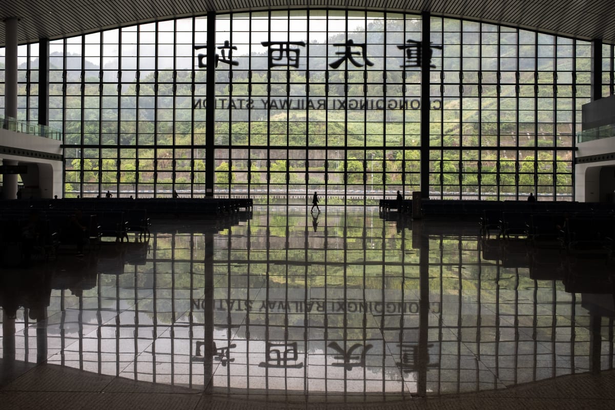 The glass wall of Chongqing West railway station mirrored in the polished floor of its empty hall — Luke Neville