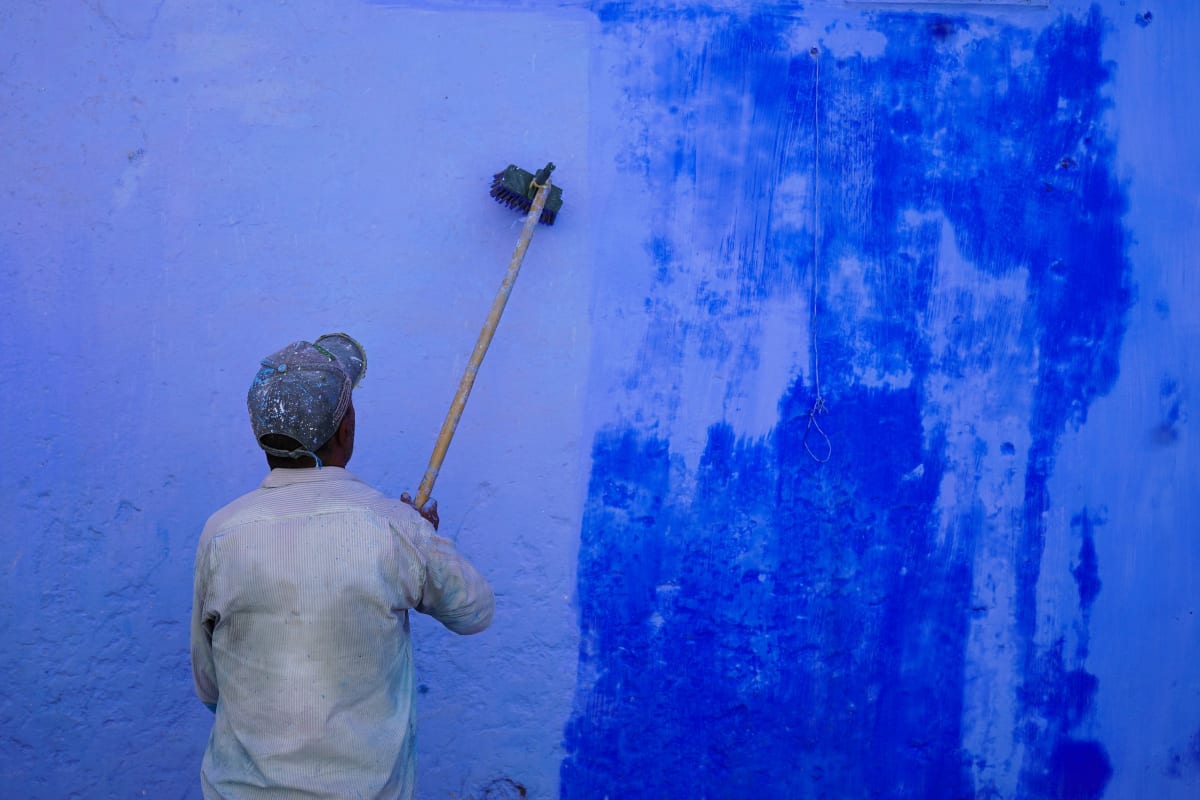 A painter rolls fresh blue paint over a weathered blue wall — Luke Neville
