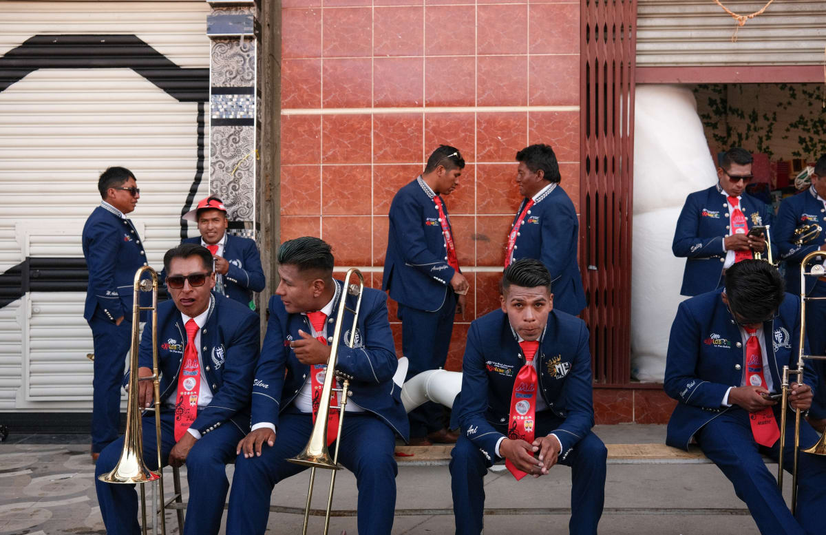 A brass band in matching blue suits and red ties waits with trombones between sets — Luke Neville