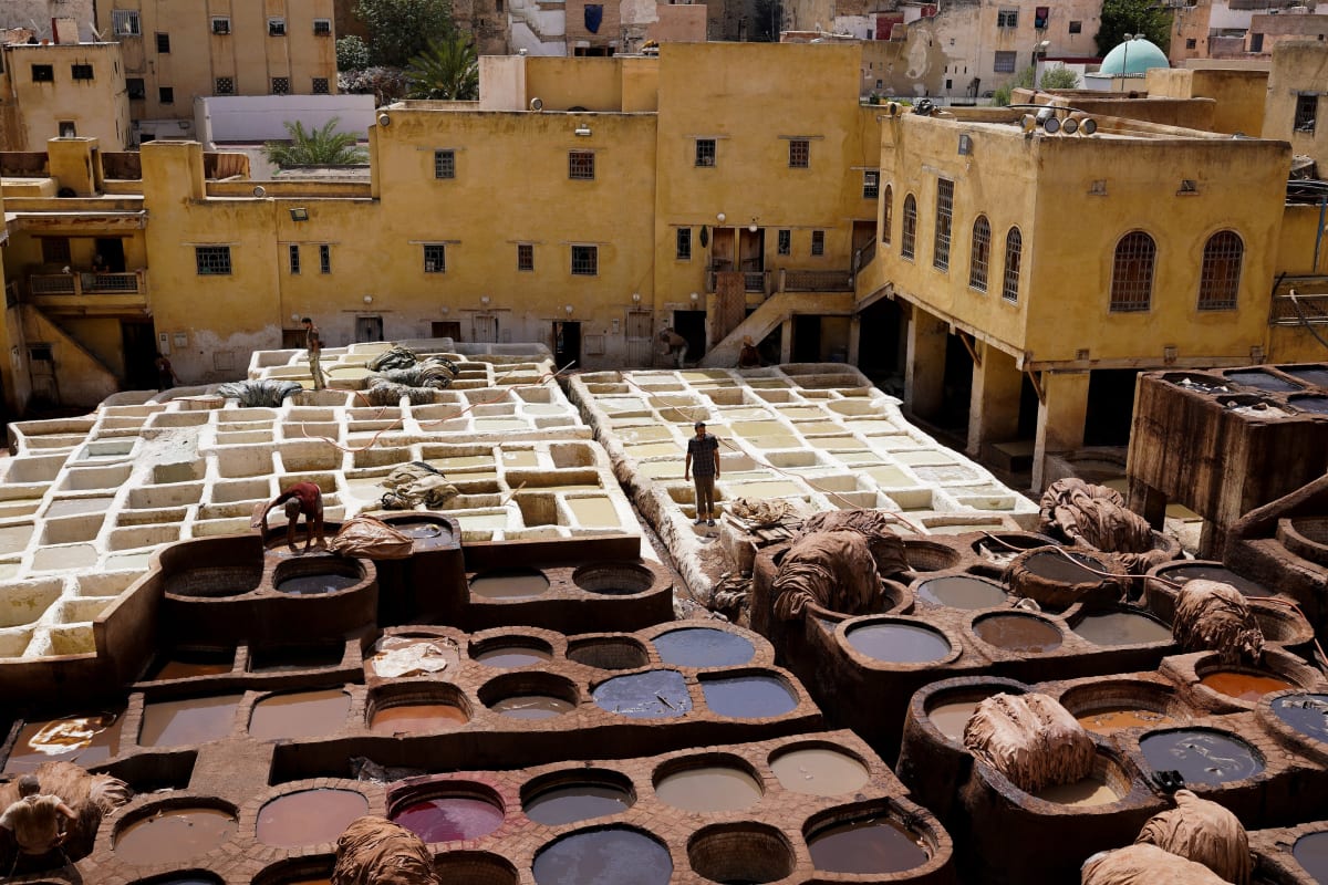 The stone dye pits of the Fes tannery spread below ochre houses, workers moving between the basins — Luke Neville