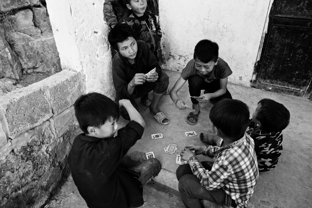 Six boys sit on the ground in the corner of a courtyard playing cards, seen from above — Dennis and Patrick Weinert
