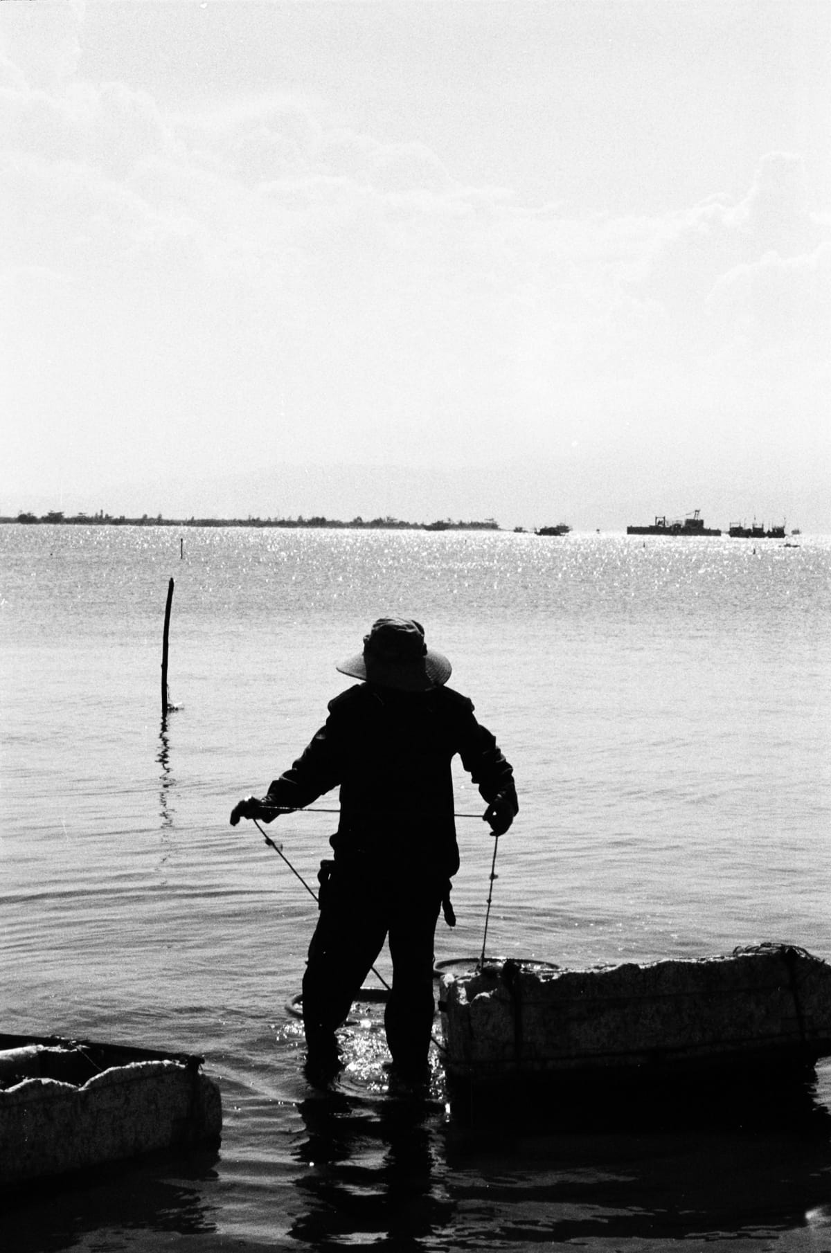 Silhouetted fisherman wades in sparkling coastal shallows pulling lines near a Vietnamese shore