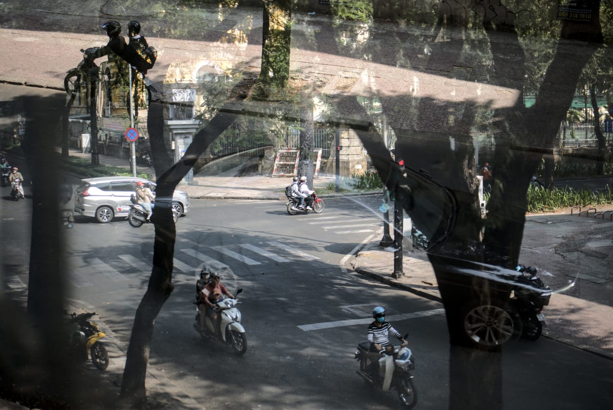 Motorbikes stream through a Ho Chi Minh City intersection seen through a glass window reflection