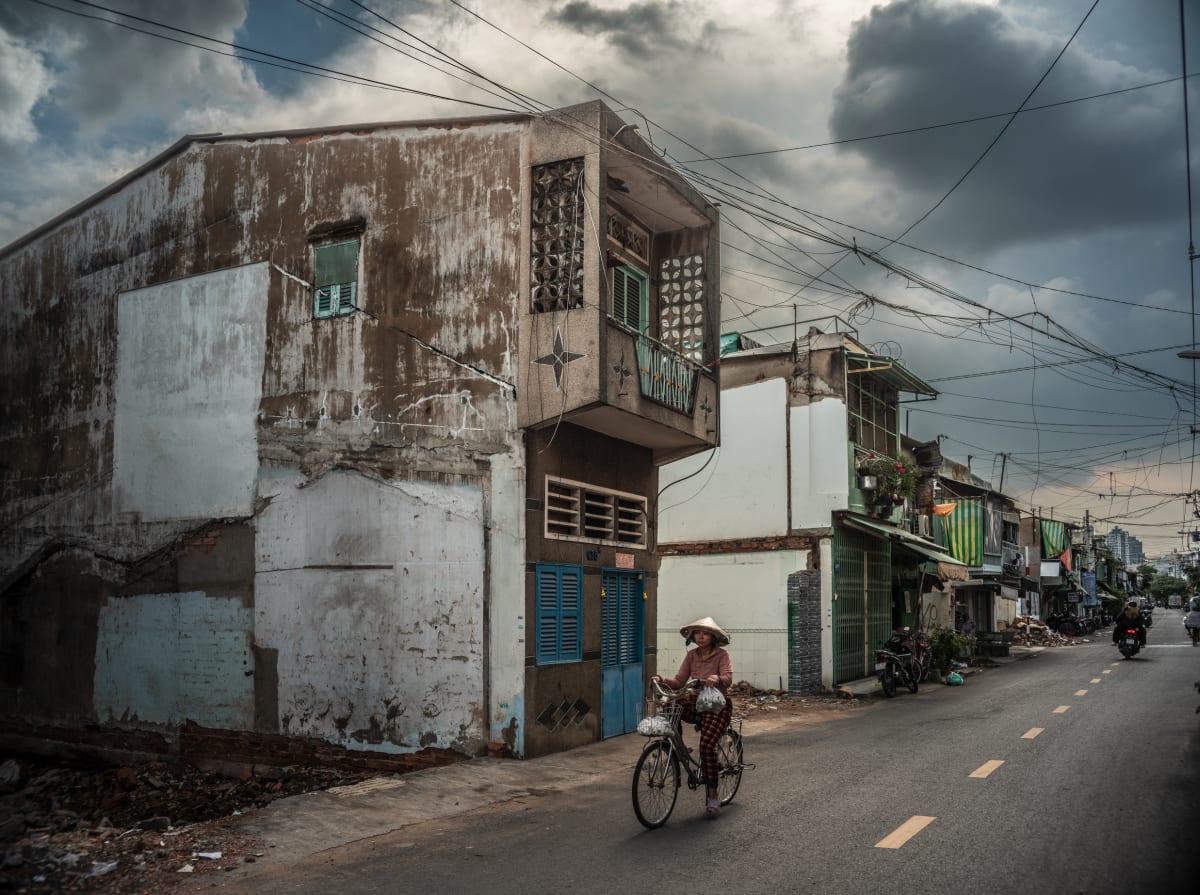 Woman cycling past weathered shophouse in District 8, Saigon — Alexandre Garel