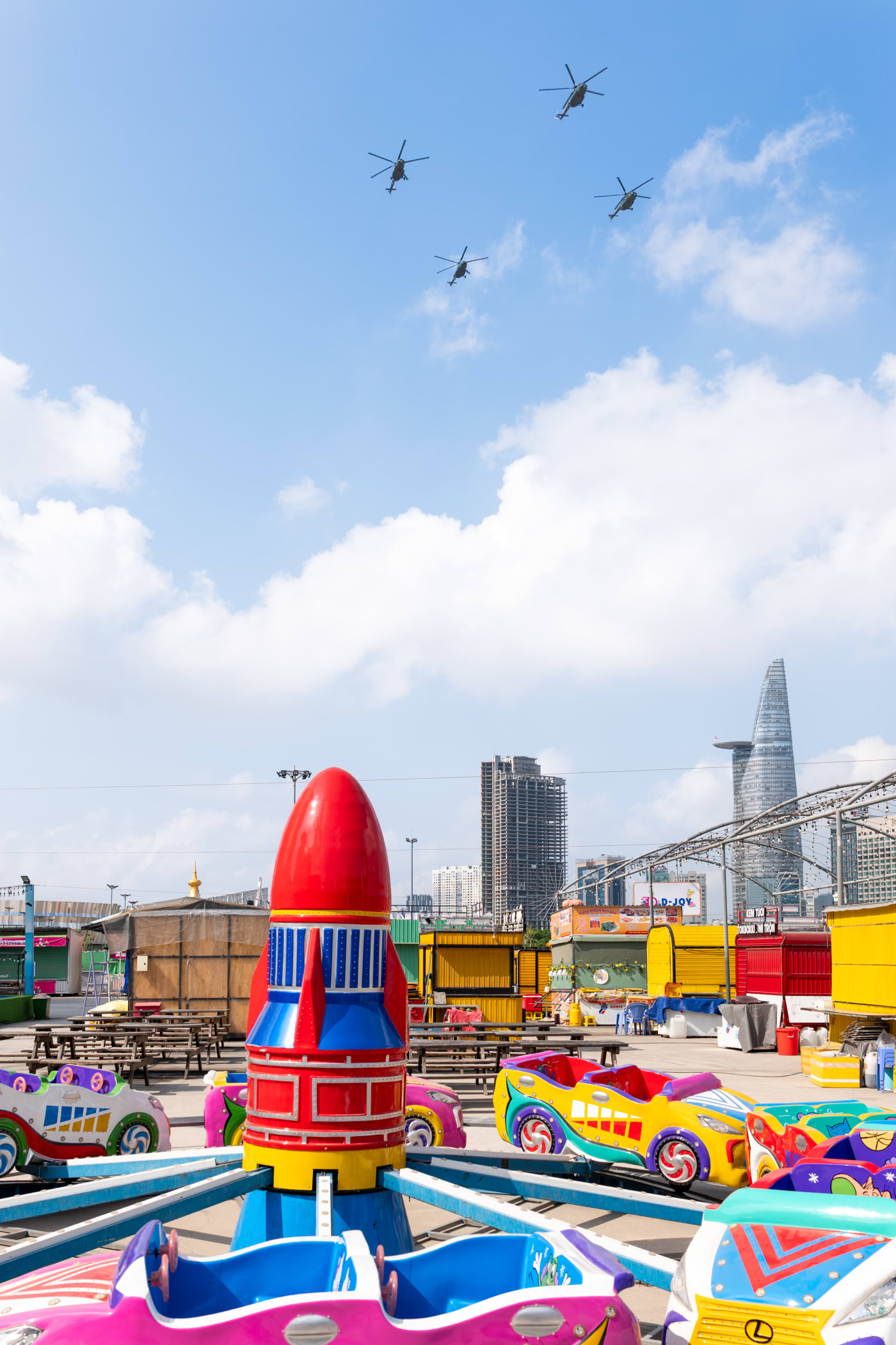 Helicopters in formation over an empty amusement park rocket ride — Le Hoang Tuan