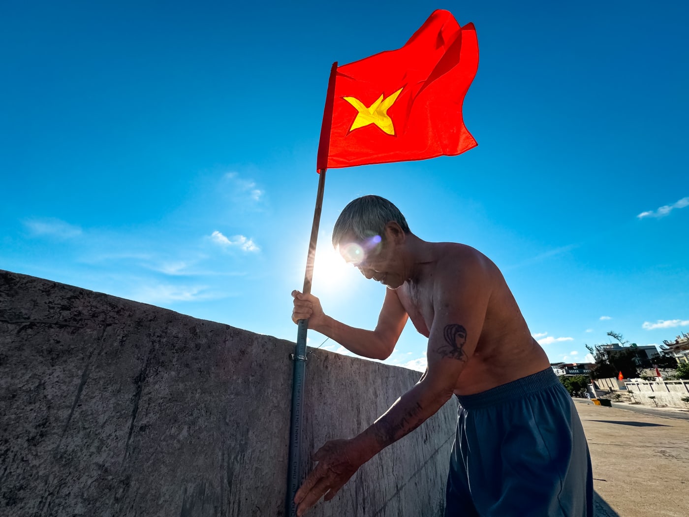 Man plants a Vietnamese flag against the midday sun — Le Hoang Tuan