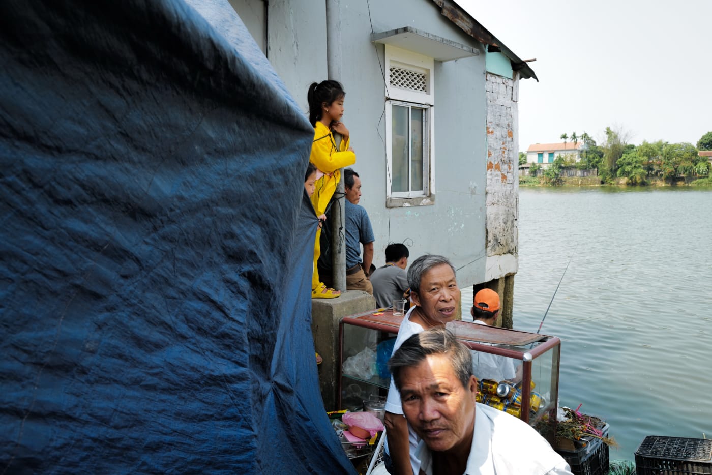 Family gathered on a stilt-house porch above the river — Le Hoang Tuan