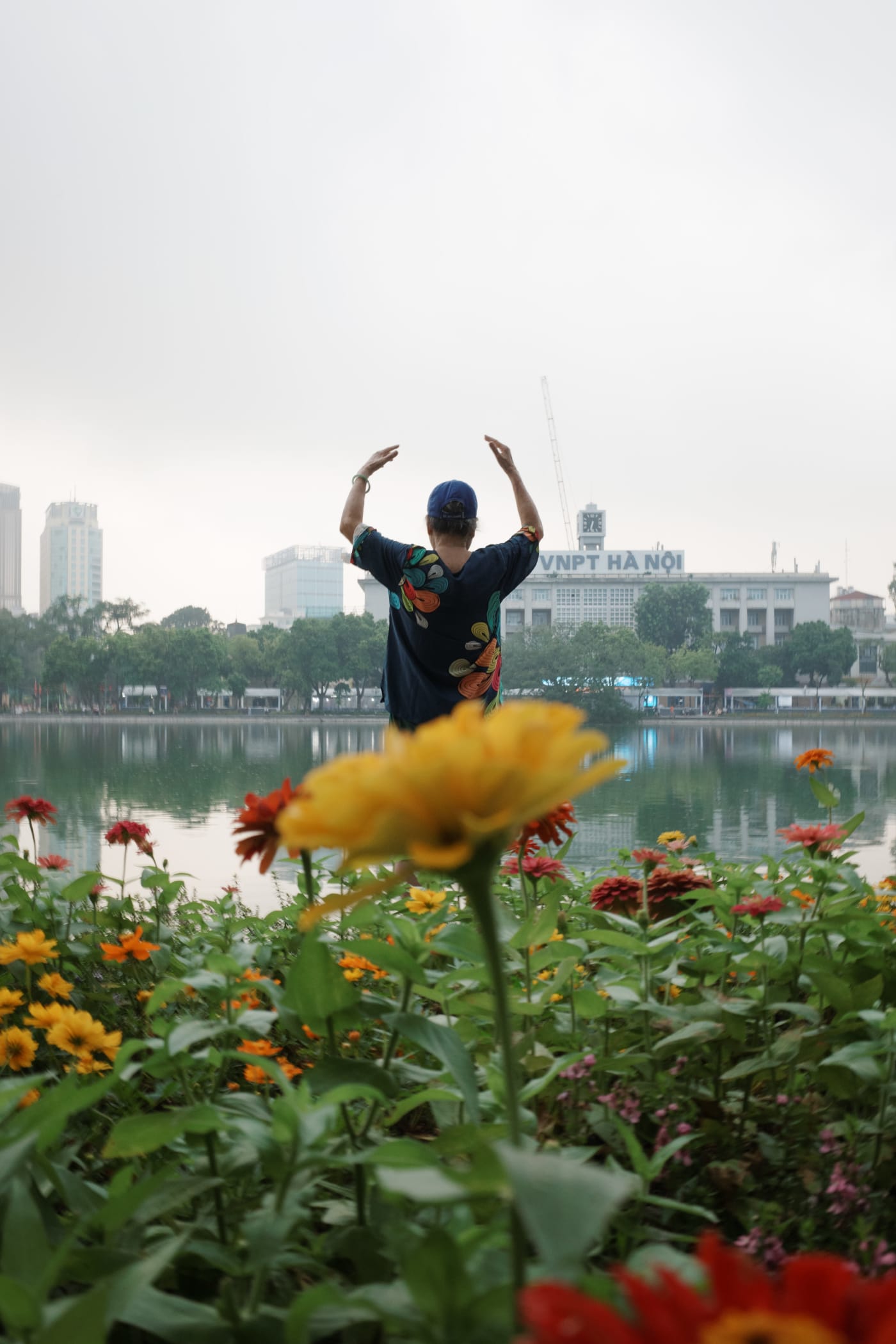 Morning tai chi behind a bed of zinnias at the lake — Le Hoang Tuan