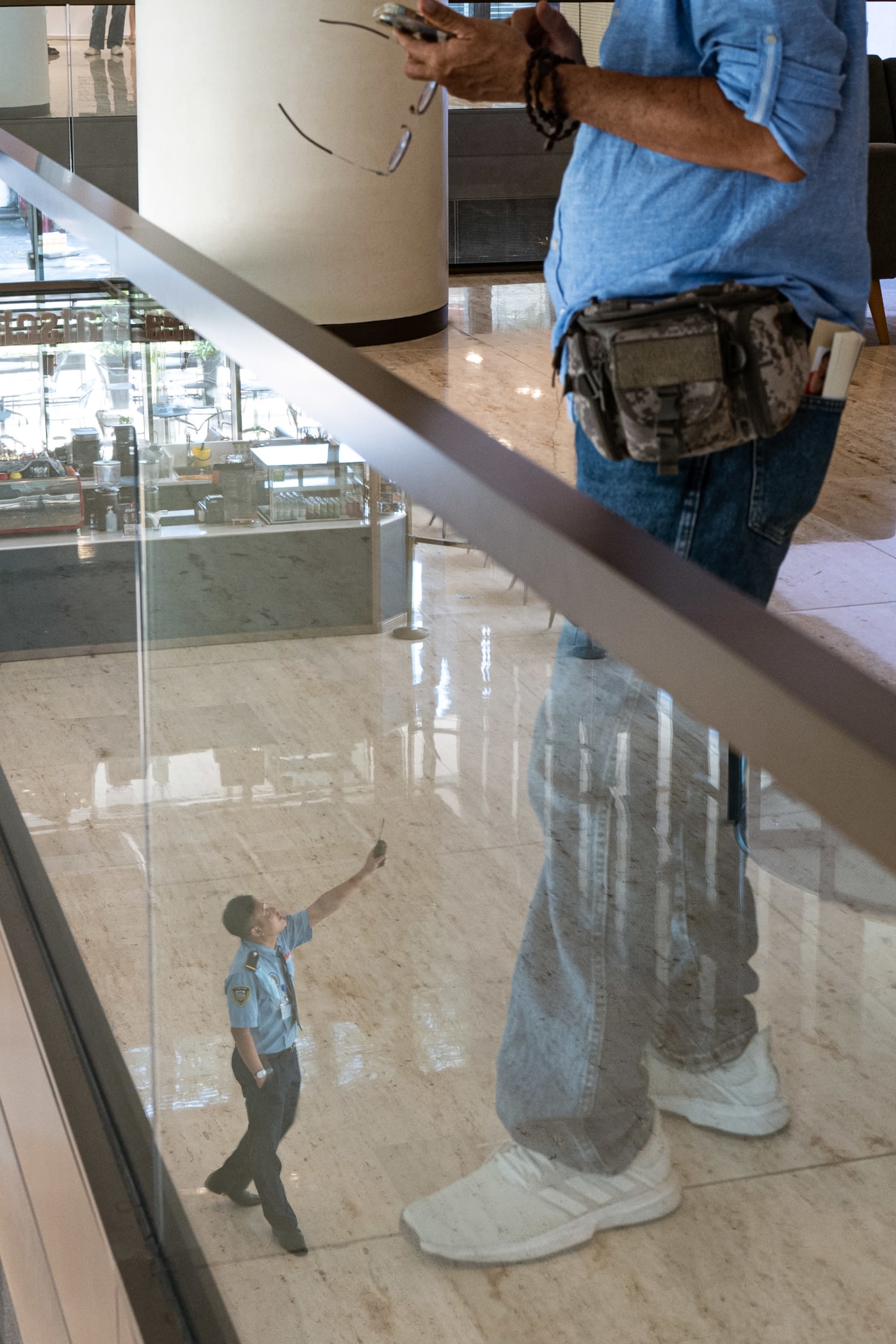Mall reflection with security guard reaching toward passerby — Le Hoang Tuan