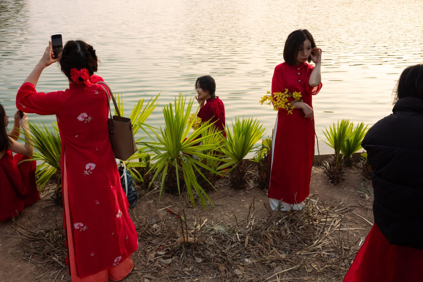Women in red áo dài photographing each other by the lake — Le Hoang Tuan