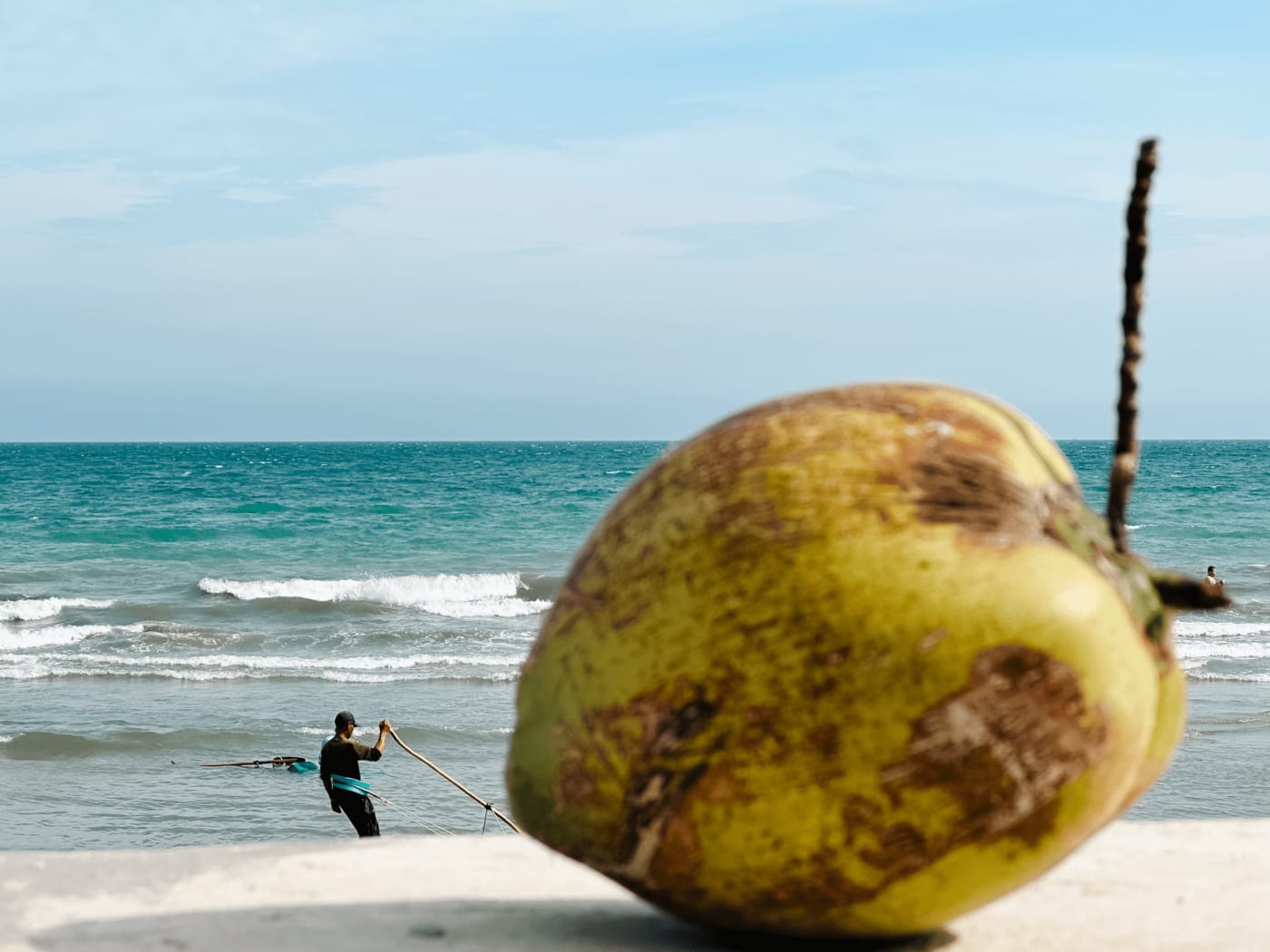 Coconut on a seawall with a fisherman working the waves behind — Le Hoang Tuan