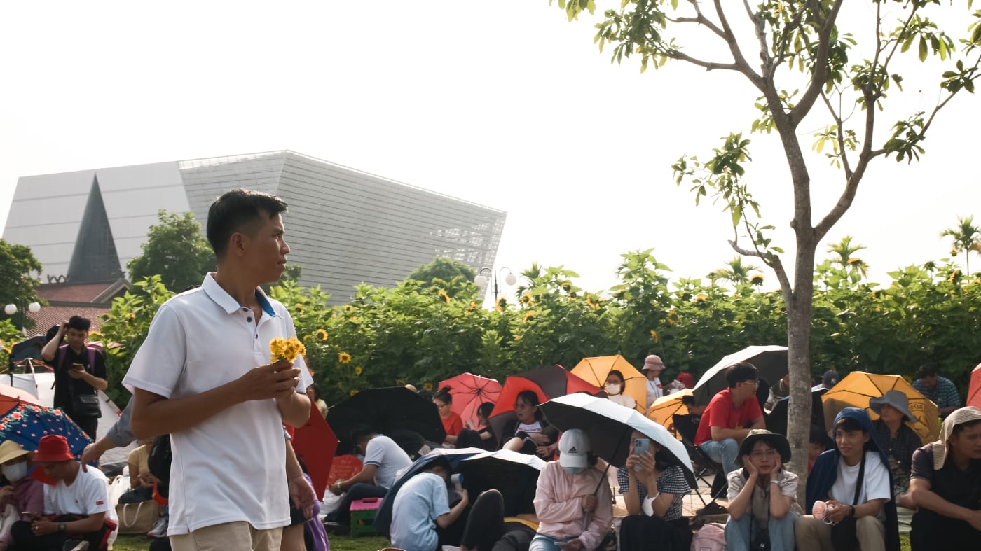 Man carries sunflowers past a crowd sheltering under umbrellas — Le Hoang Tuan