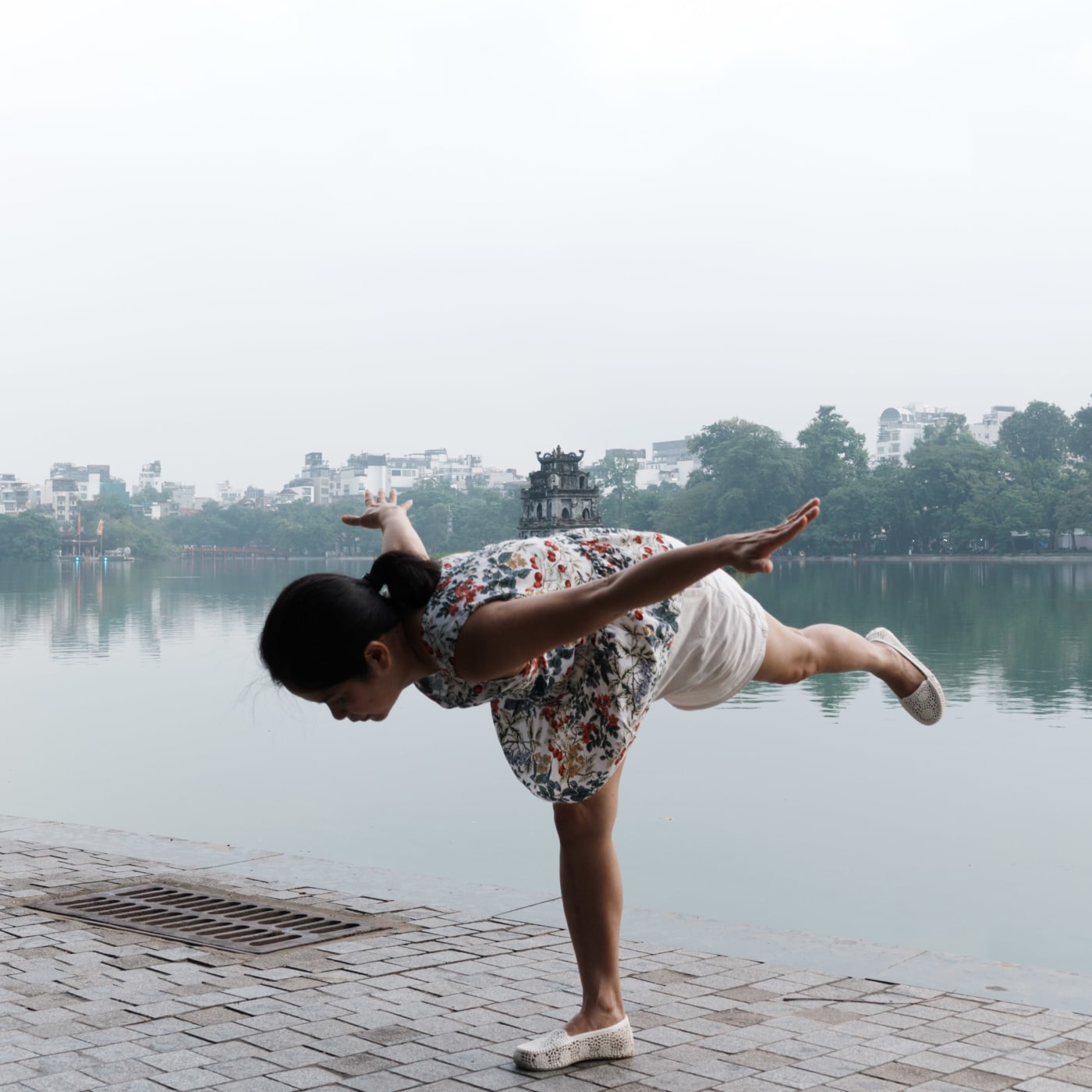 Woman doing yoga pose by Hoan Kiem Lake with Turtle Tower — Le Hoang Tuan