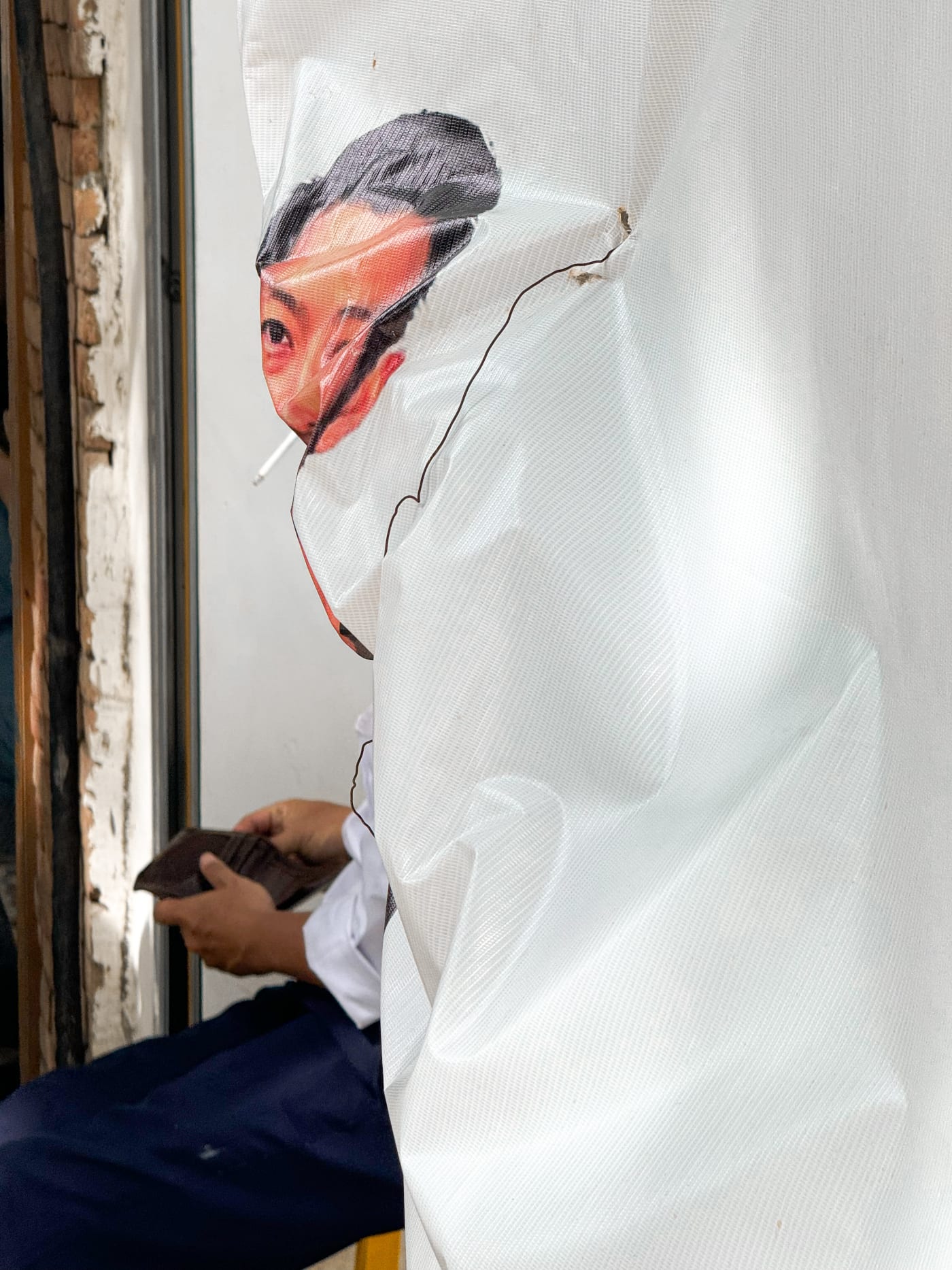Cigarette tucked into a face printed on a torn banner — Le Hoang Tuan