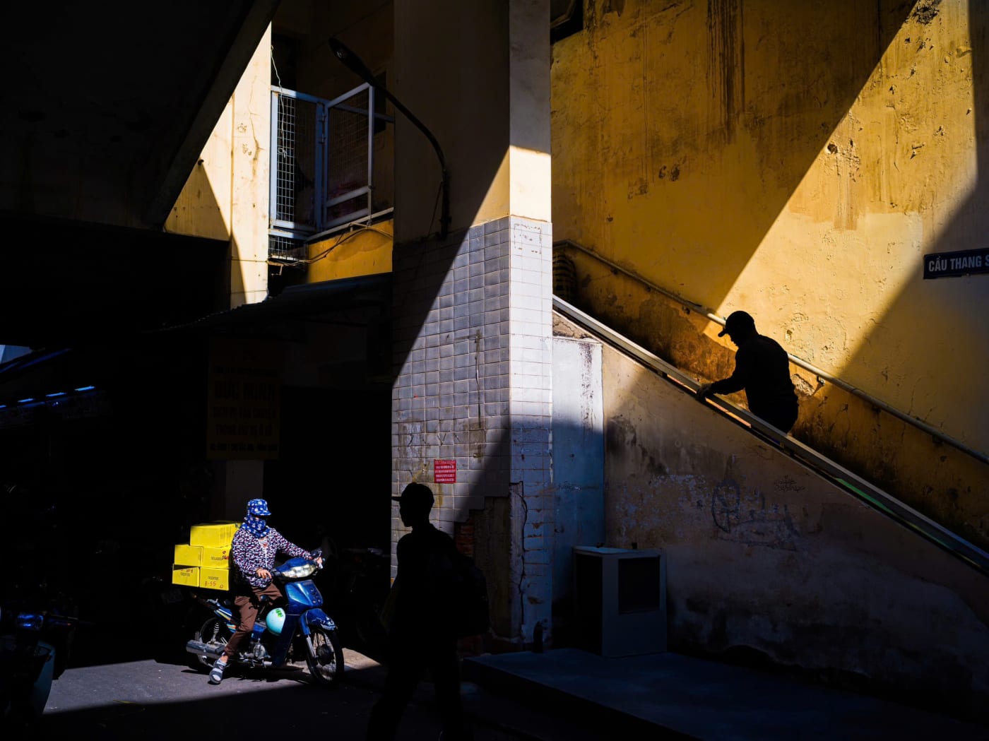 Golden light beams cut through an old apartment stairwell as a silhouette climbs the stairs — MatDat.Ng