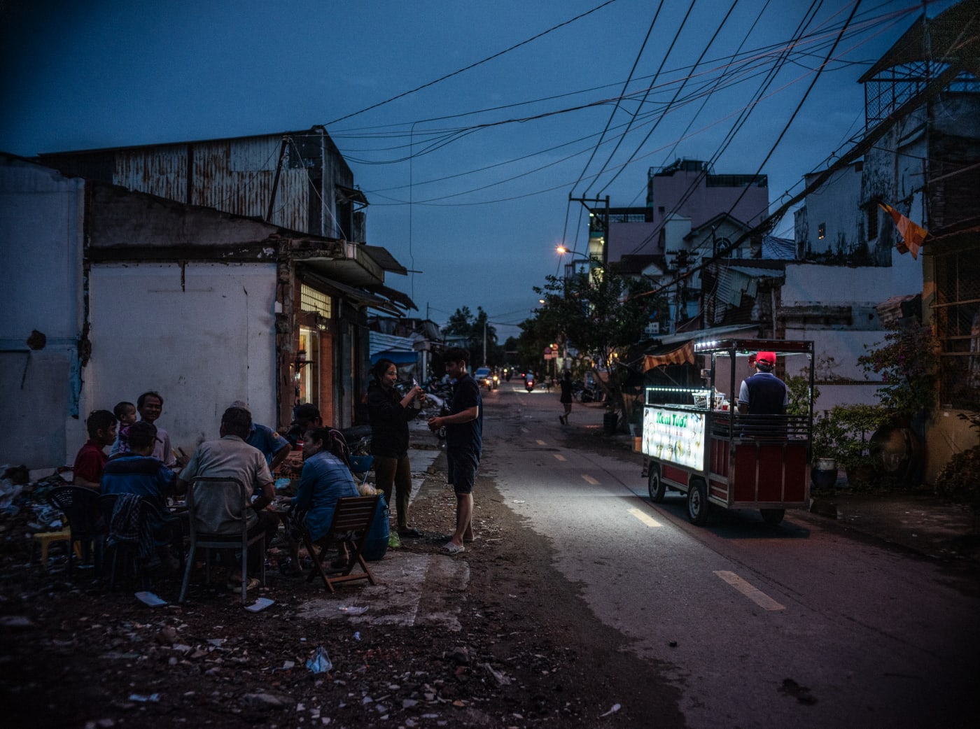 Blue hour street scene with food cart and neighbours gathering, District 8 — Alexandre Garel